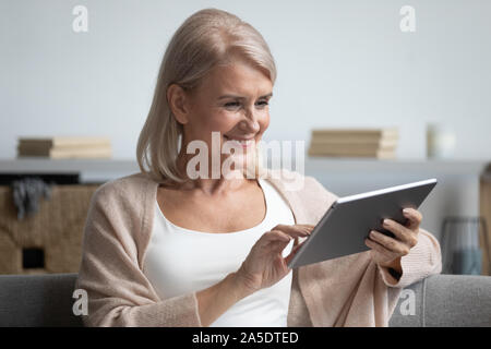 Happy middle aged woman using tablet computer at home Stock Photo