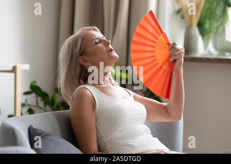 Stressed old woman waving fan suffer from overheating at home Stock Photo