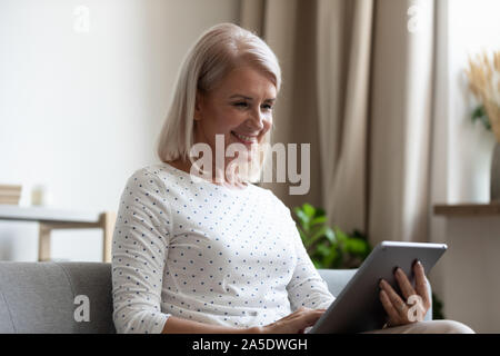 Smiling old woman holding using digital tablet relaxing at home Stock Photo