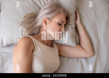 Peaceful healthy mature woman lying asleep in bed, top view Stock Photo