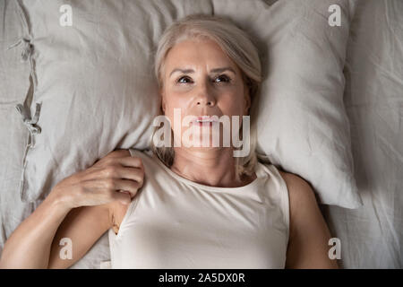 Middle aged woman insomniac lying awake in bed, top view Stock Photo