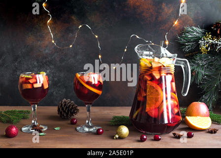 Christmas Punch or Sangria in pitcher and glasses with Christmas decoration on wooden table, copy space. Red wine fruit Christmas drink. Stock Photo