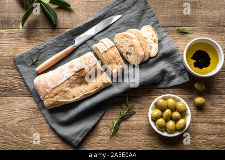 Ciabatta - Fresh Homemade Italian Bread, olives and olive oil on wooden table, top view. Stock Photo