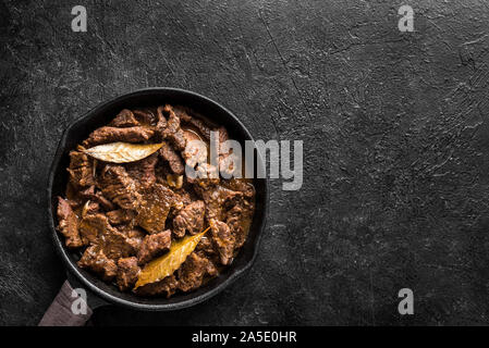 Meat Stew. Beef stewed in red wine sauce, top view, copy space. Roasted beef meat. Braised beef portion meat. Slow cooked meat in cast iron pan. Stock Photo