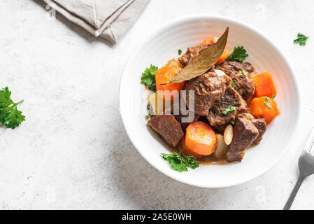 Beef meat stewed with potatoes, carrots and spices on white background, close up. Homemade winter comfort food - slow cooked meat stew. Stock Photo
