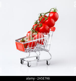 Mini shopping cart with cherry tomatoes on light gray background, shallow DOF. Stock Photo