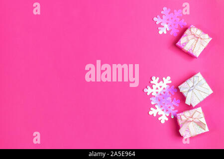Three shiny gift boxes with bows and iridescent plastic purple snowflakes on bright pink background. Christmas festive presents. Top view, copy space. Stock Photo