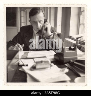 Photo of stressed older middle aged man working management, manager, managing / in office using telephone circa 1950's, U.K. Stock Photo