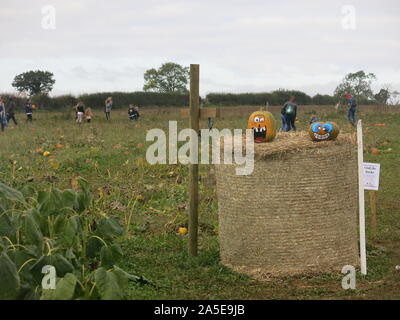Two carved and decorated pumpkins sit on a large bale of straw at the entrance to an English pick your own pumpkin farm; October 2019 Stock Photo