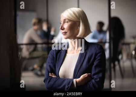 Thoughtful old businesswoman ceo looking through window thinking of leadership Stock Photo