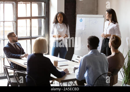 Diverse female coaches team give flip chart presentation at training Stock Photo