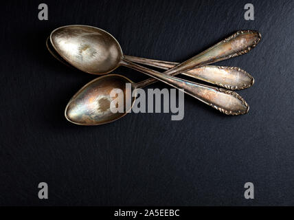 three old and worn teaspoons stacked on a slate board, free space for text Stock Photo