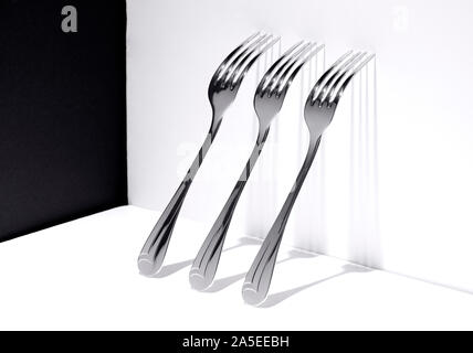 three forks resting on a white wall with the shadow cast on this, conceptual photo Stock Photo