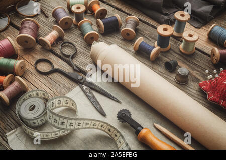 Sewing items: retro tailoring scissors, measuring tape, thimble, wooden spools of thread, patterns on paper, cutting knife, cushion for including pins