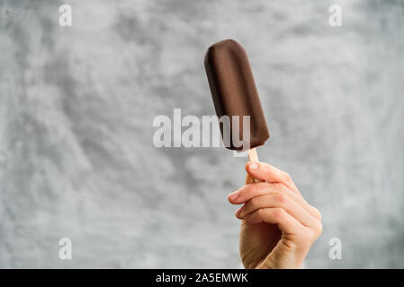Woman holding Eskimo pie ice cream in hand on gray background. Eskimo pie day concept Stock Photo