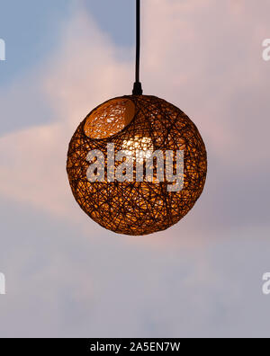A woven shade with lamp hanging on the background of sunset sky. Space for text Stock Photo