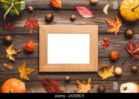 Blank photo frame with thanksgiving autumn composition. Frame made of pumpkins, fall leaves, flowers and nuts on rustic wooden table. Flat lay, top vi Stock Photo