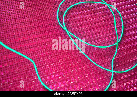 Green glowing wire, cold neon, electroluminescent cord, cable lies on a holographic pink background with various types of overflow. Stock Photo