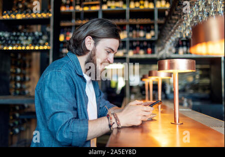 Young brown-haired bearded man using smartphone by a bar Stock Photo
