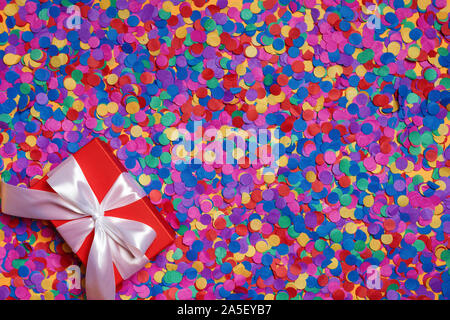 Red box with a gift on scattered confetti. Top view. Stock Photo
