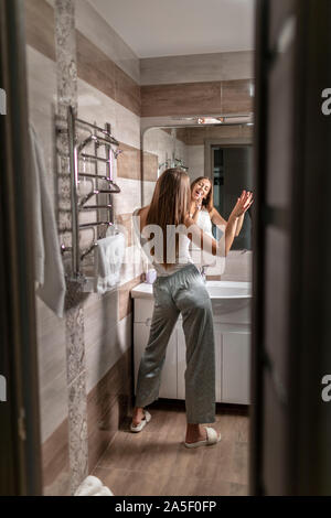 Young beautiful woman brushing teeth and singing as if the toothbrush is a microphone Stock Photo