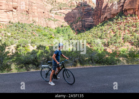 Springdale, USA - August 6, 2019: Zion National Park road in Utah with high angle view of people man riding bicycle by desert landscape Stock Photo