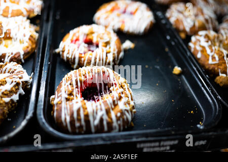White glaze iced danish pastry fried donuts with red purple raspberry jam on tray in fresh bakery store shop closeup Stock Photo