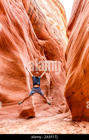 Man happy hiker jumping up vertical view by red wave shape formations at Antelope slot canyon in Arizona on footpath trail from Lake Powell Stock Photo