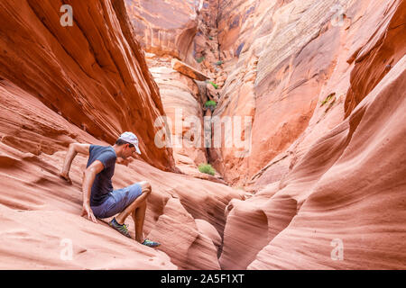 Orange red wave sandstone abstract formations and man climbing rocks at narrow Antelope slot canyon in Arizona on trail from Lake Powell
