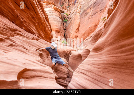 Orange red wave sandstone formations and man climbing crossing rocks at narrow Antelope slot canyon in Arizona on trail from Lake Powell