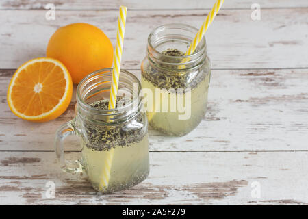 Chia seeds detox water. Healthy beverage with orange fruit slice in manson glass jars and drinking straw on wooden table with orange fruits. Stock Photo