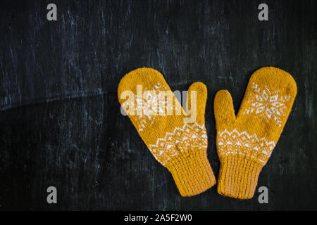 a pair of yellow orange knitted mittens on a dark blue-green-brown wooden Stock Photo