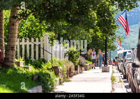 Telluride, USA - August 14, 2019: Vacation town village in Colorado with sidewalk pavement and young couple walking on sunny summer day by American fl Stock Photo