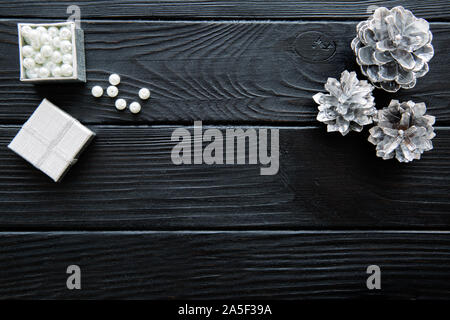 Silver pine cones and white beads on black table, space for text, copy-space. Top view, wooden background. Stock Photo
