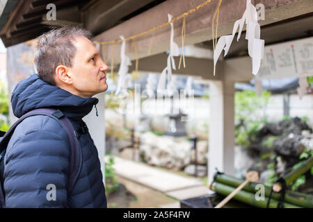 Shinjuku, Tokyo, Japan shrine with one tourist man praying by purification fountain and hanging shide paper on rome in city Stock Photo