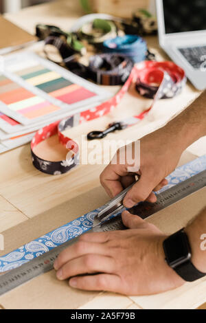Hands of young creative designer using handtools while preparing decorative workpieces for handmade pet collars Stock Photo