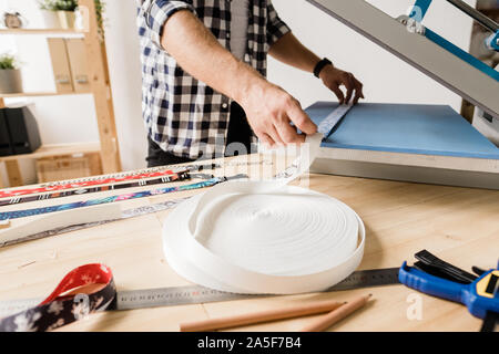 Young designer using new equipment for printing ornaments on handmade pet collars while standing by table Stock Photo