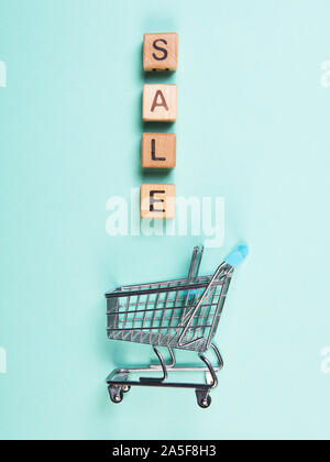 A miniature shopping cart and wooden blocks with the wordings SALE, isolated against mint background. Stock Photo