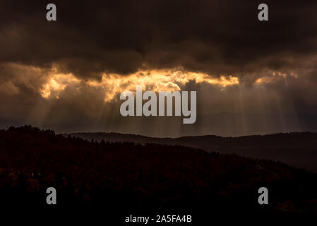 Dark clouds and sun rays. Autumn forest hills on rainy day Stock Photo