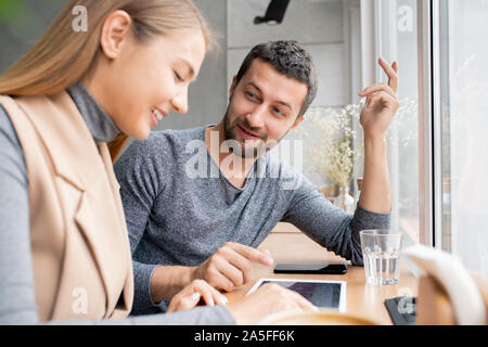 Happy young couple choosing goods in online shop and discussing prices while spending time in cafe Stock Photo