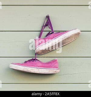 Pair of red old wornout sneakers hanging on the wall, weathered abandoned casual shoes Stock Photo