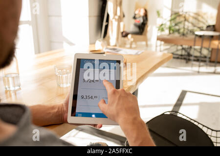 Young man pointing at financial information on touchpad display while checking his balance in personal bank Stock Photo