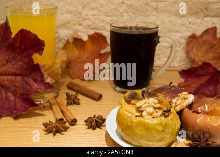 Mulled red wine with healthy dessert, baked apples with honey and nuts. Decorated with dried colorful leaves, cinnamon rolls and anise stars. Close up Stock Photo