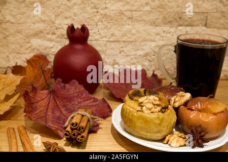 Hot mulled wine and baked apples with spices, honey, cinnamon, cloves and anise stars, autumn scene with colorful dried leaves on bricks wall backgrou Stock Photo