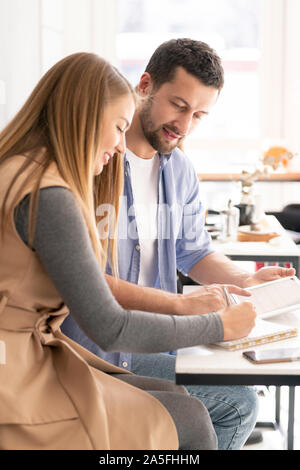 Two young contemporary employees sitting by table in office or cafe while planning work and discussing ideas Stock Photo