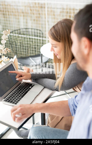 Young confident businesswoman pointing at data on laptop display while explaining working table to colleague Stock Photo