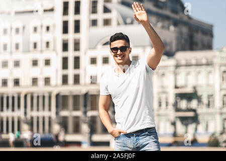 Outdoors Leisure. Stylish guy in sunglasses standing on the street waving to friend smiling happy Stock Photo
