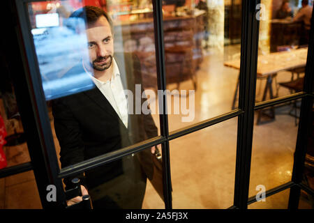 High angle portrait of handsome mature gentleman leaving luxury restaurant standing by glass door, copy space Stock Photo