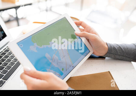 Hands of young female student holding digital tablet with map on display while preparing homework or working over project Stock Photo