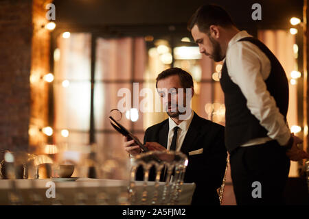 Portrait of mature bearded businessman looking at menu while ordering dinner in luxury restaurant, copy space Stock Photo